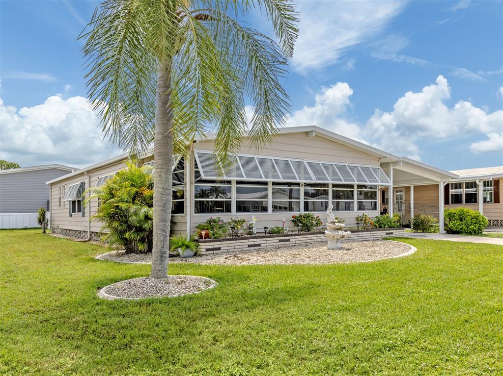 A single-story manufactured home with a palm tree, gravel landscaping, and a covered carport — 182 PALM HARBOR DRIVE, NORTH PORT, FL