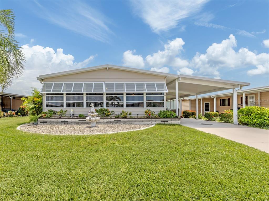 A single-story manufactured home with a carport, a front lawn, and a decorative fountain — 182 PALM HARBOR DRIVE, NORTH PORT, FL