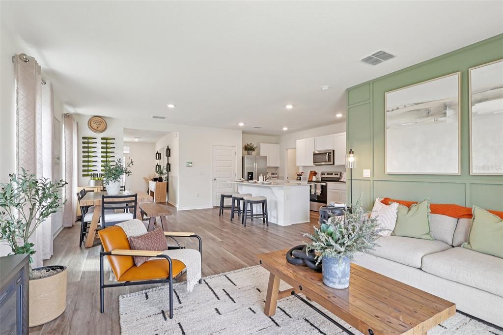 An open-concept living room and kitchen featuring wood-look flooring and a green paneled accent wall — 4214 BIXBY BRIDGE PLACE, DAVENPORT, FL
