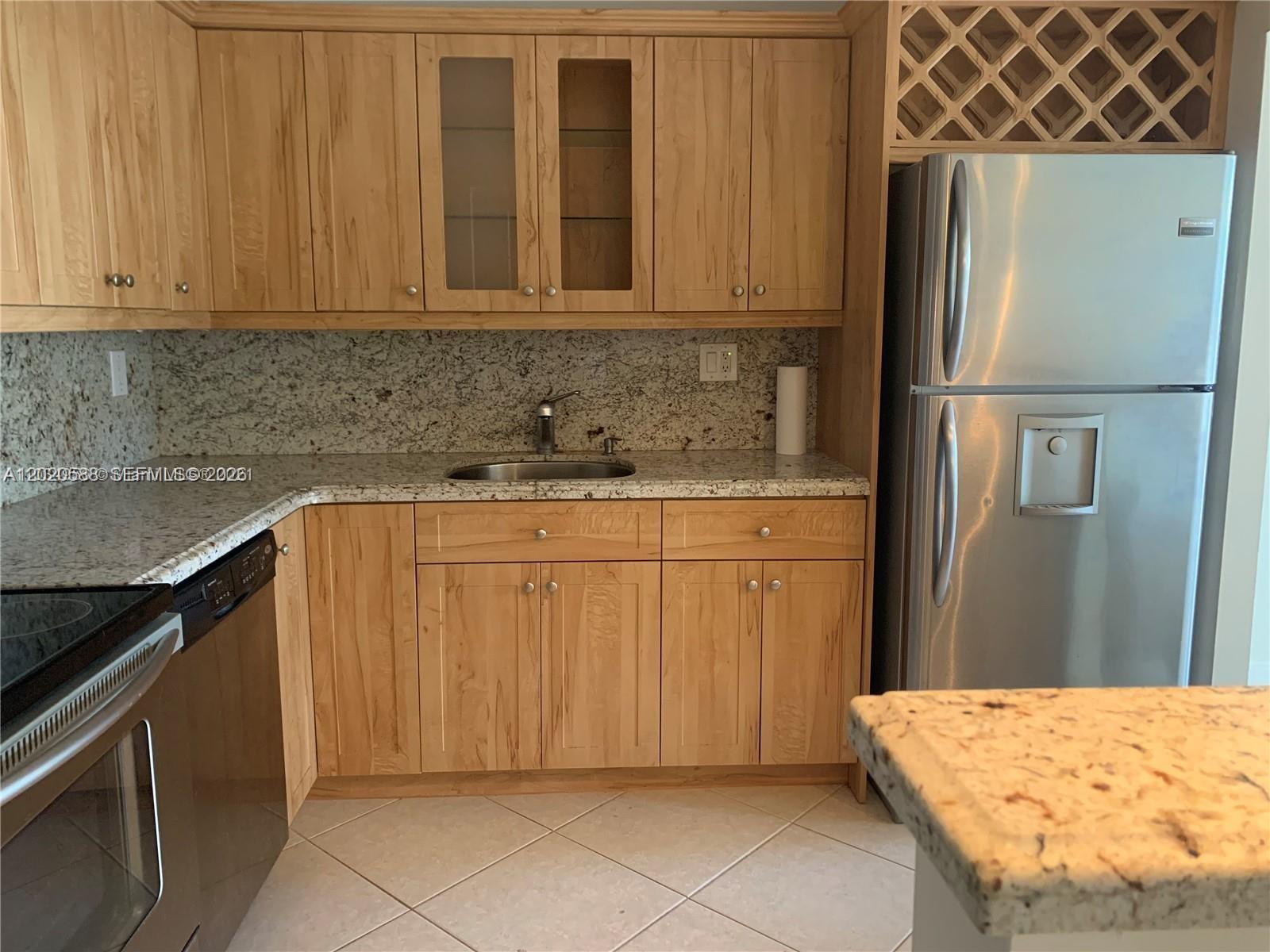 A kitchen features light wood cabinets, granite countertops, a stainless steel refrigerator, and tile flooring — 2731 Taft St # 311, Hollywood FL 33020, HOLLYWOOD, FL
