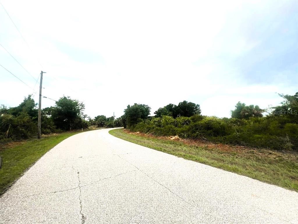 A paved road curves through a rural area with dense trees and vegetation — 7441 MANVILLE TERRACE, PORT CHARLOTTE, FL