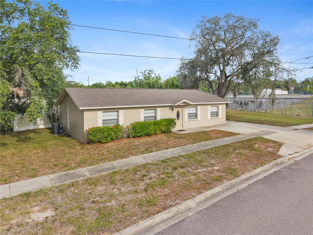 A single-story tan brick house with a shingled roof sits on a grassy corner lot — 1221 E COURT STREET, TARPON SPRINGS, FL