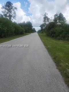 A paved road stretches into the distance, flanked by trees and grassy shoulders — 437 Naples AVE S, Lehigh Acres FL 33974, LEHIGH ACRES, FL