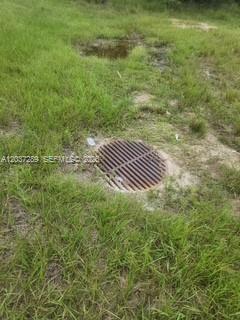 A circular metal storm drain grate is set into the grass in an outdoor area — 437 Naples AVE S, Lehigh Acres FL 33974, LEHIGH ACRES, FL