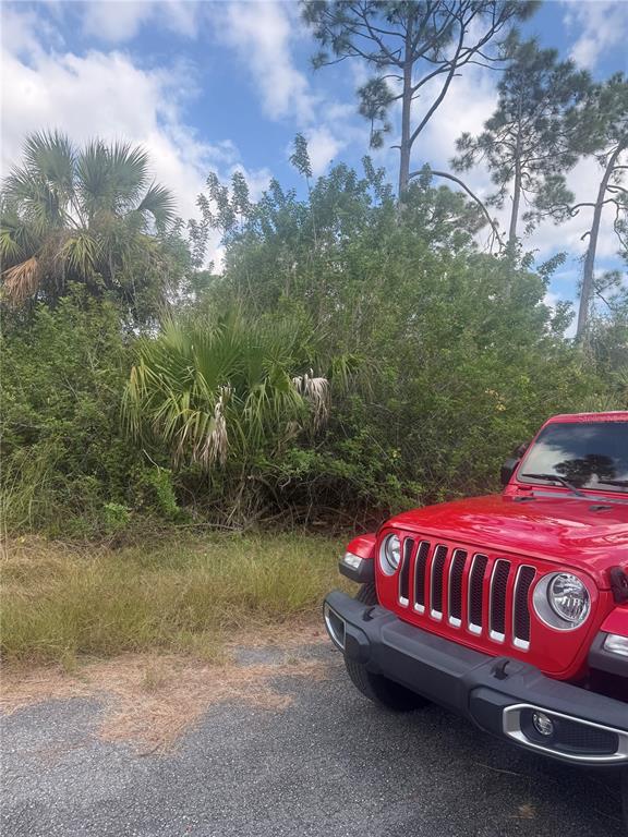 A red Jeep is parked on a paved surface in front of dense Florida vegetation — Lot 15 COASTAL STREET, NORTH PORT, FL