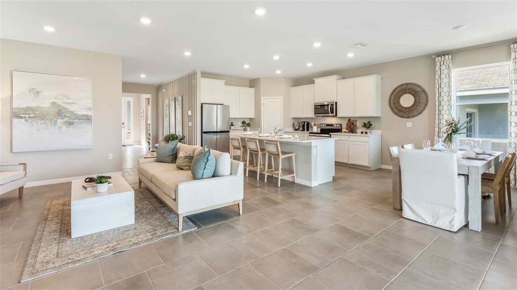 An open-concept living room and kitchen feature white cabinetry, tile flooring, and neutral furniture — 3507 HARVEST GARDENS LOOP, PLANT CITY, FL