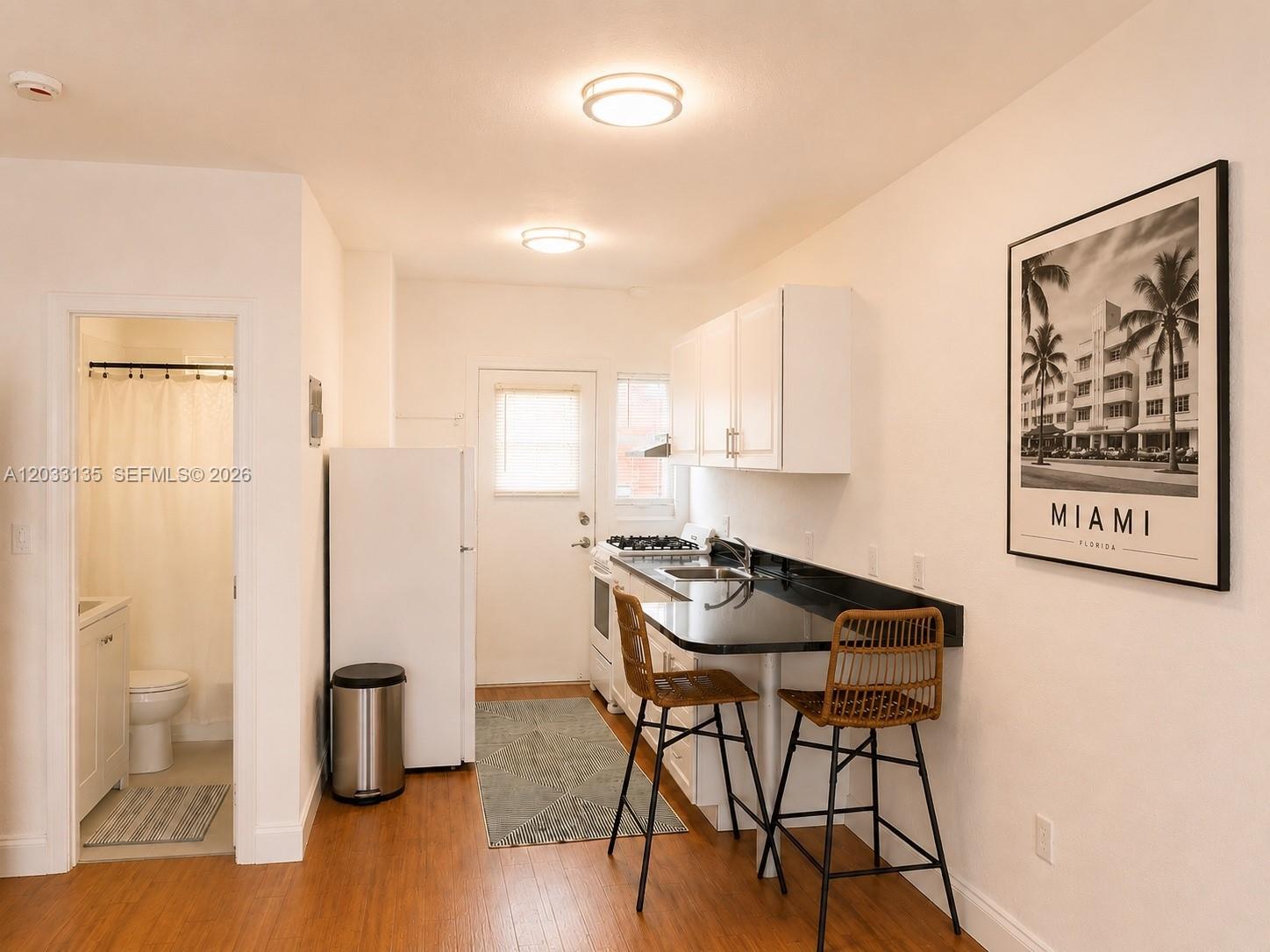 A small kitchen features white cabinets, black countertops, a breakfast bar, and an adjacent bathroom — 300 74th St # 5, Miami Beach FL 33141, MIAMI BEACH, FL