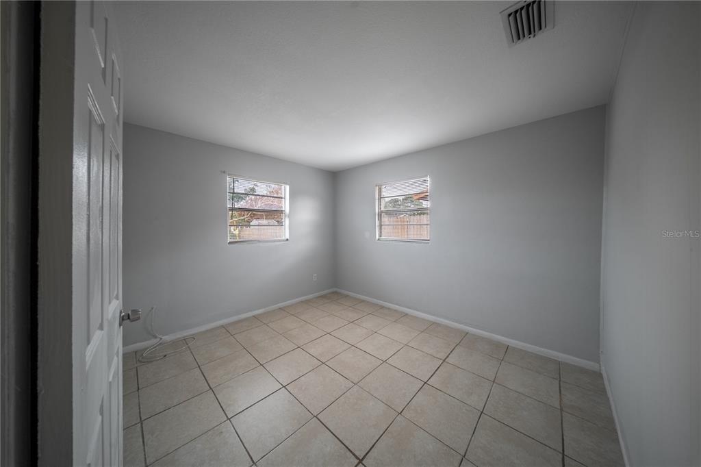 An empty bedroom features light gray walls, beige tile flooring, and two windows — 1706 N 29TH STREET, FORT PIERCE, FL