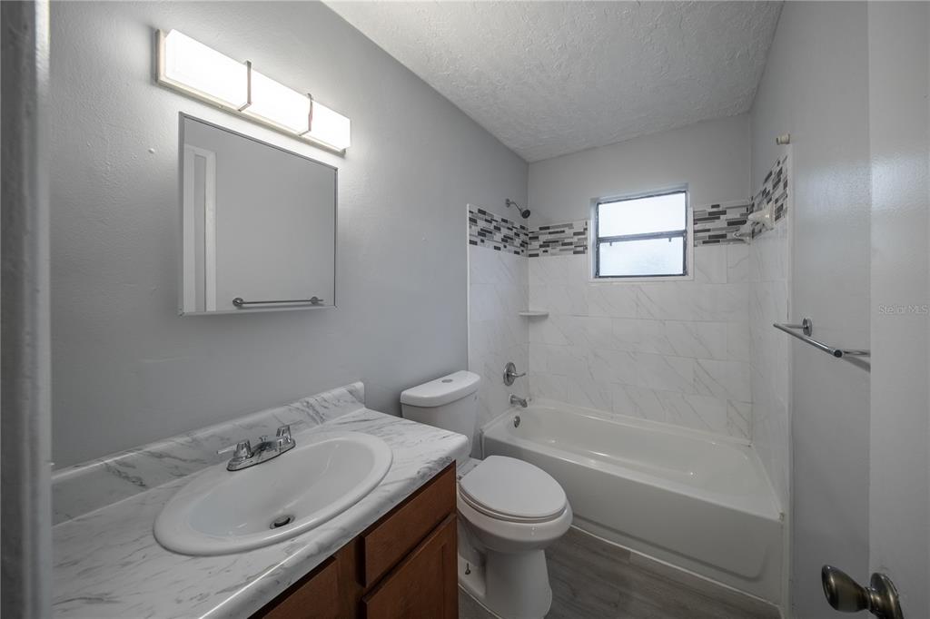 A bathroom features a vanity with a marble-look countertop, a toilet, and a tiled tub-shower — 1706 N 29TH STREET, FORT PIERCE, FL