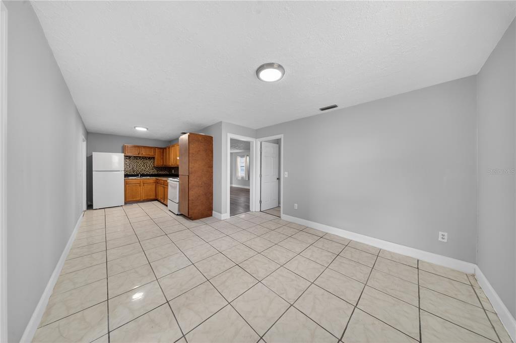 A kitchen with light-colored tile flooring, wooden cabinets, and white appliances opens to a room — 1706 N 29TH STREET, FORT PIERCE, FL