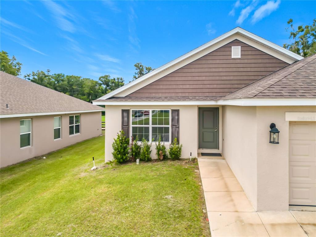 A beige single-story house with a brown shingled roof, a front door, and a garage — 187 NW 45TH LOOP, OCALA, FL