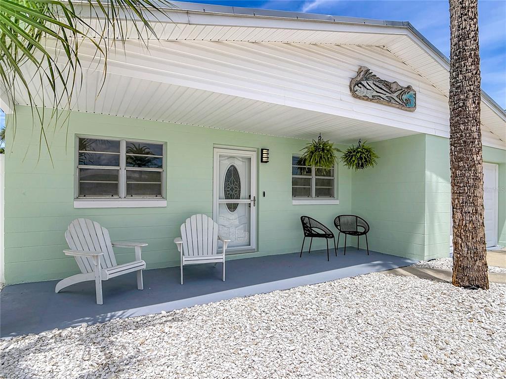 A light green house exterior features a covered porch with white chairs and a fish decoration — 220 CRAWFORD ROAD, NEW SMYRNA BEACH, FL