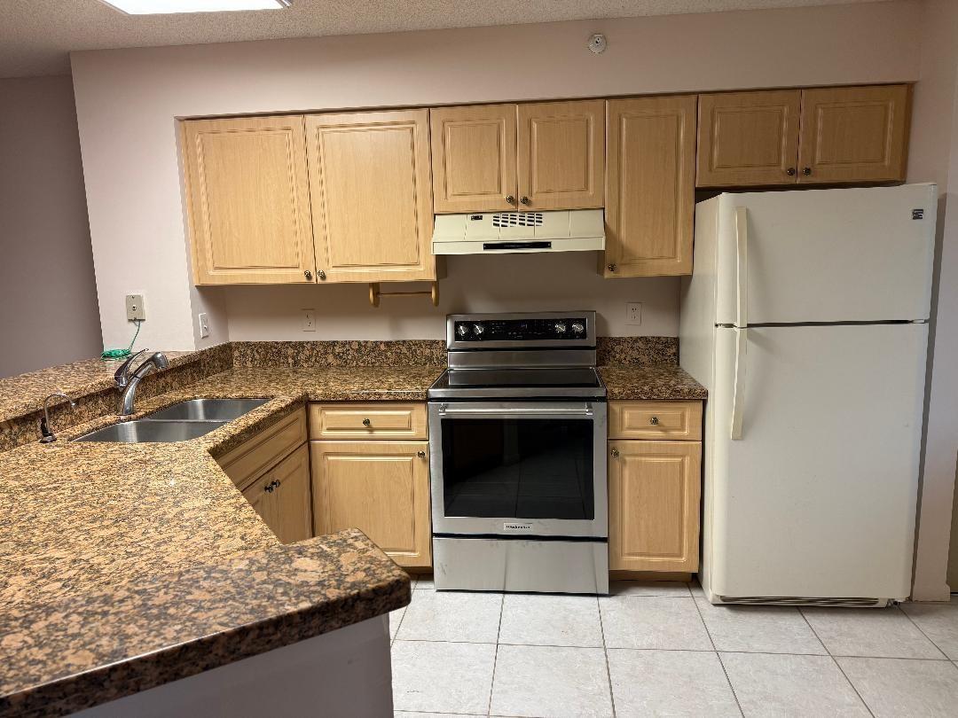 A kitchen with light wood cabinets, granite countertops, a stainless steel stove, and white refrigerator — 2205 S Cypress Bend Drive # 307, Pompano Beach FL 33069, POMPANO BEACH, FL