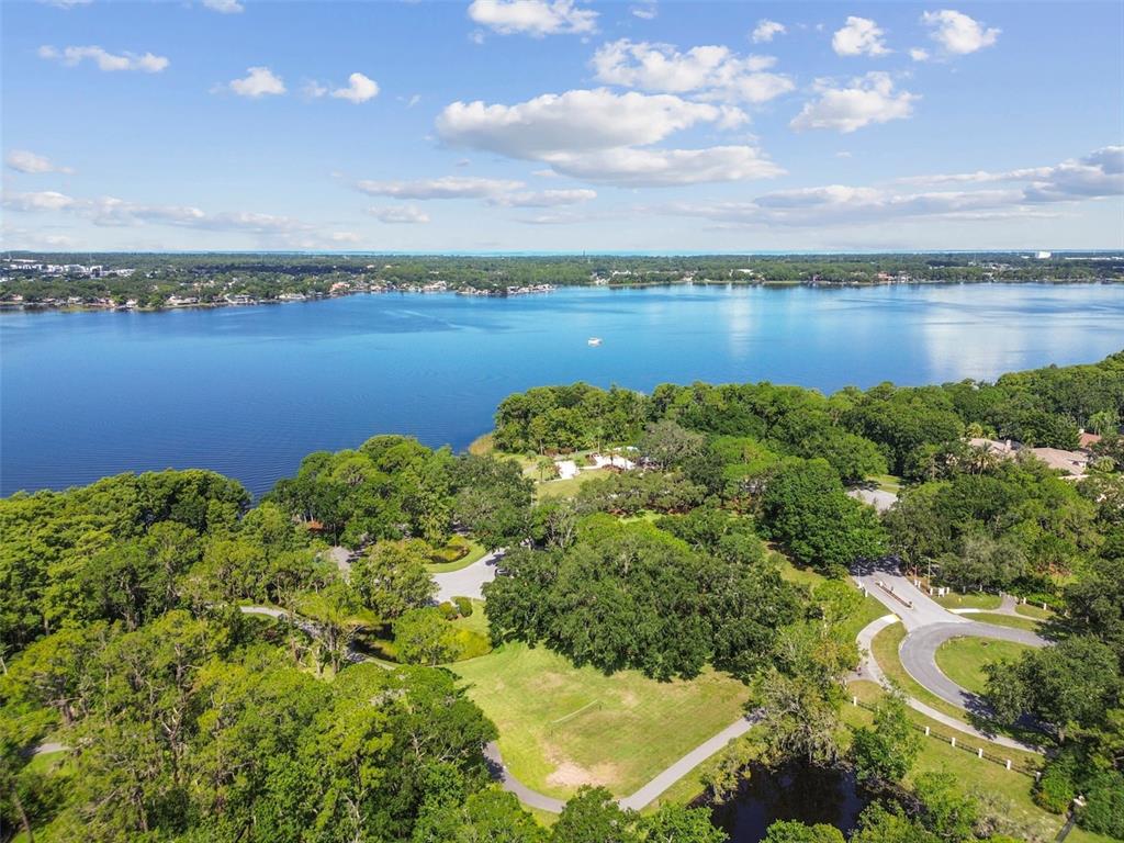 An aerial view shows a large lake bordered by dense trees and a paved path — 3025 NAUGHTON WAY, TARPON SPRINGS, FL