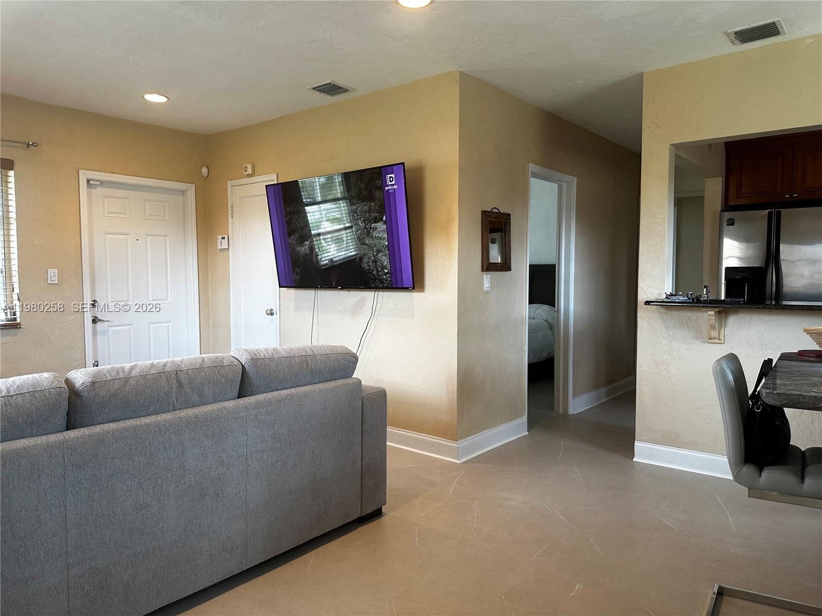 A living room features a gray sofa, a wall-mounted television, and an adjacent kitchen area — 7540 SW 37th St, Miami FL 33155, MIAMI, FL