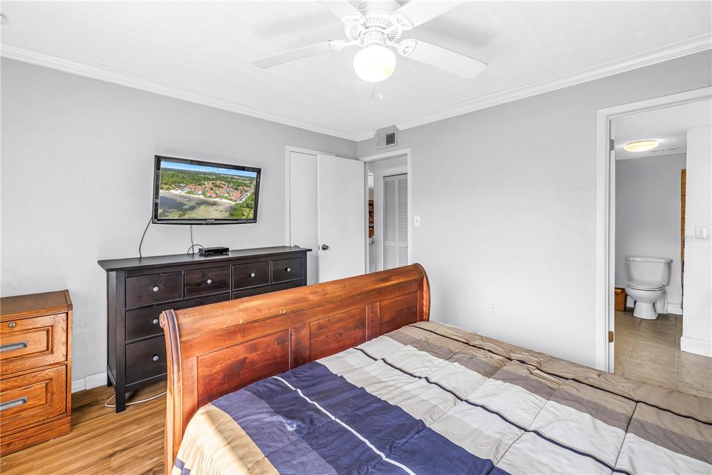 A bedroom features a wooden bed frame, a dark dresser with a television, and an attached bathroom — 3580 41ST LANE S UNIT I, ST PETERSBURG, FL