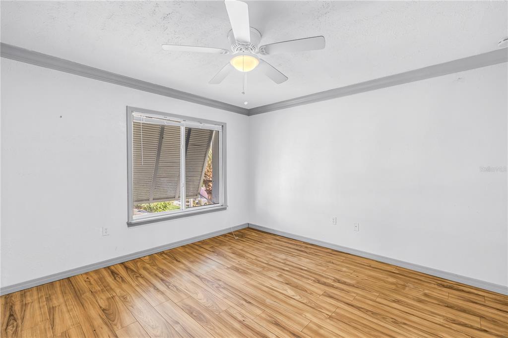 An empty bedroom features light wood-look flooring, white walls, gray trim, and a ceiling fan — 3580 41ST LANE S UNIT I, ST PETERSBURG, FL