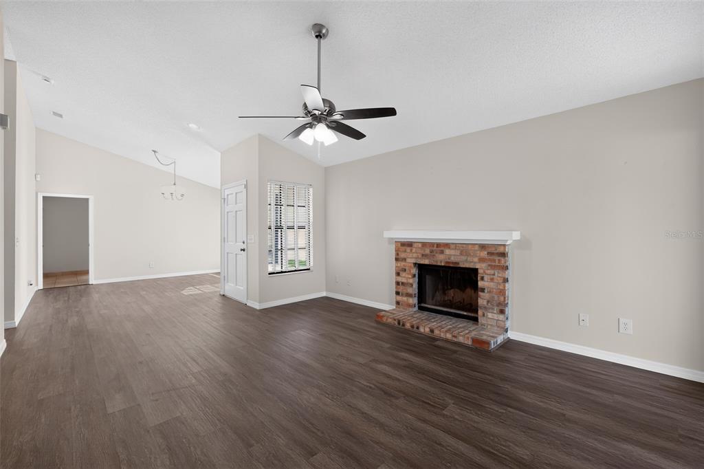 A living room features dark wood-look flooring, a brick fireplace, and a ceiling fan — 5024 CYPRESS TRACE DRIVE, TAMPA, FL