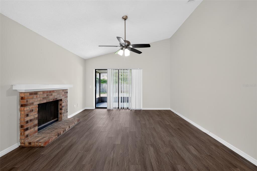 A living room with a brick fireplace, ceiling fan, and sliding glass doors to a patio — 5024 CYPRESS TRACE DRIVE, TAMPA, FL