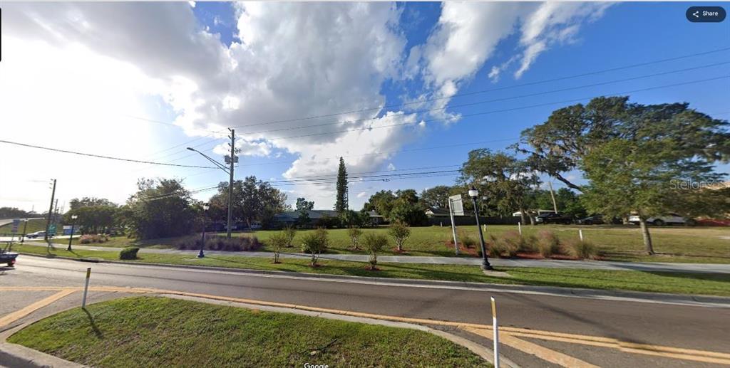 A grassy vacant lot sits along a paved road under a bright, cloudy sky — N/A, POLK CITY, FL