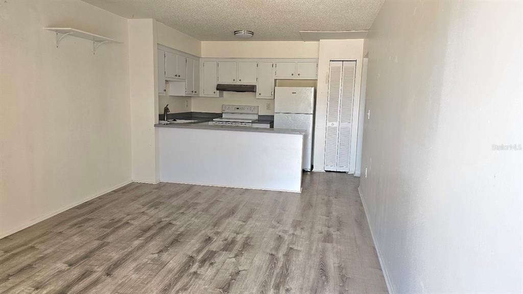 An open-concept kitchen with white cabinets and appliances overlooks a living area with wood flooring — 21150 GERTRUDE AVENUE UNIT 2, PORT CHARLOTTE, FL