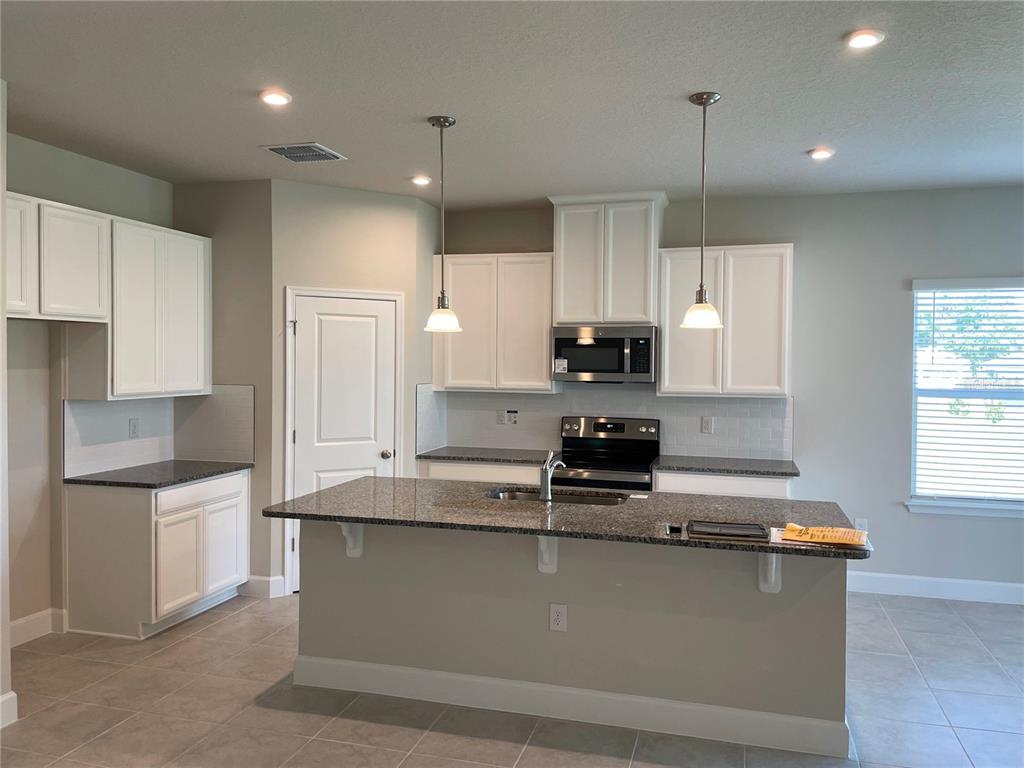 A kitchen features white cabinets, granite countertops, a center island, and stainless steel appliances — 333 WINTER BLISS LANE, MOUNT DORA, FL