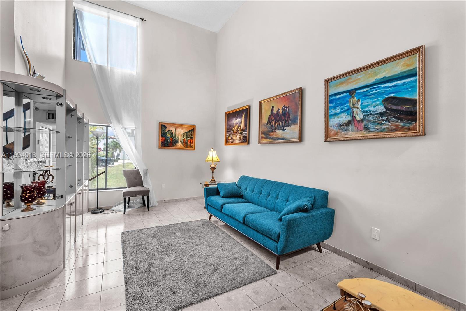 A living room features a blue sofa, a gray rug, and multiple paintings on the wall — 1321 SW 124th Ct # A, Miami FL 33184, MIAMI, FL