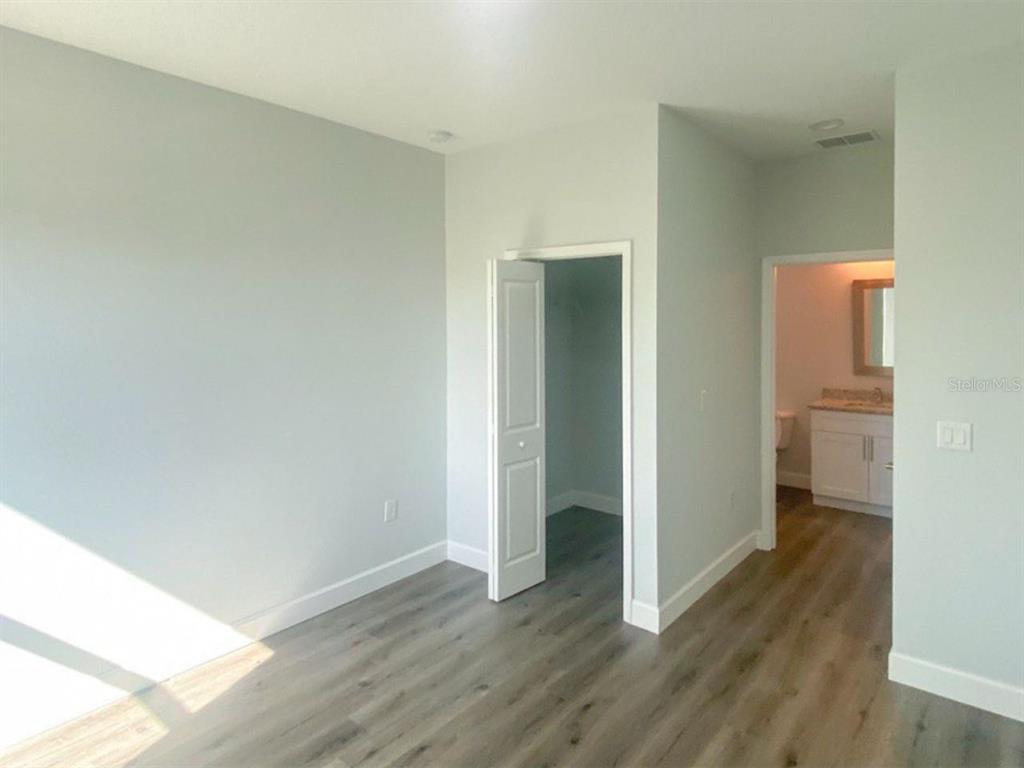 A bedroom with light gray walls, wood-look flooring, a closet, and an attached bathroom — 9163 AGATE STREET UNIT 9163, PORT CHARLOTTE, FL
