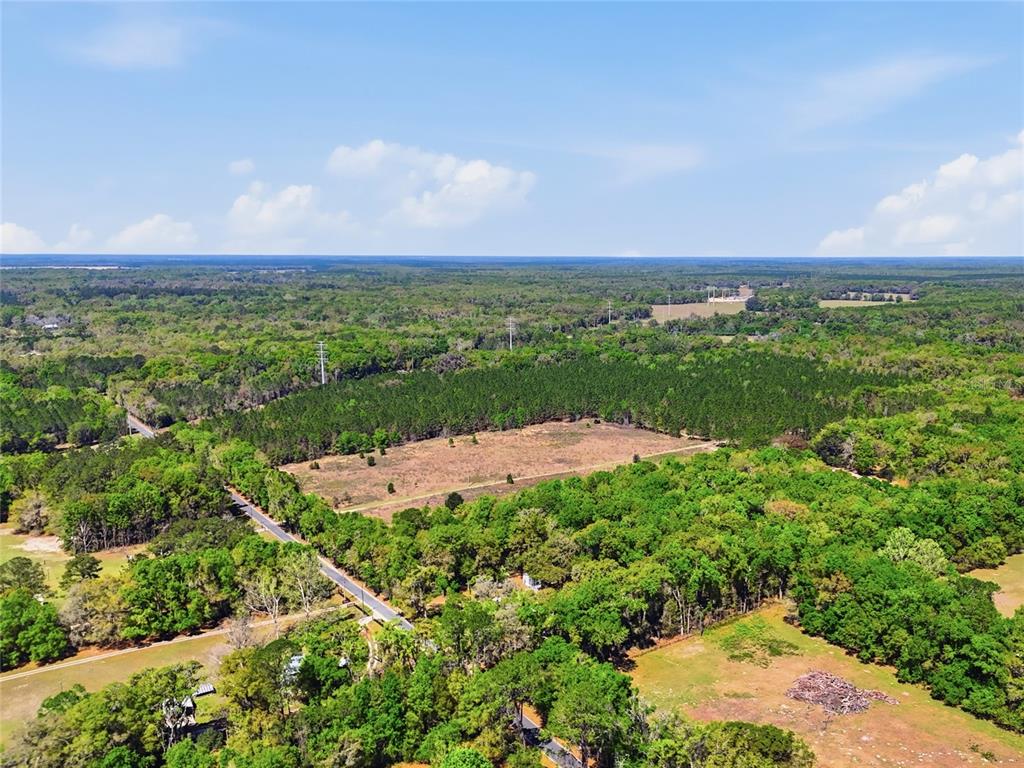 An aerial view shows a large, partially cleared plot of land surrounded by dense forest — 11791 SW 143 STREET, ARCHER, FL