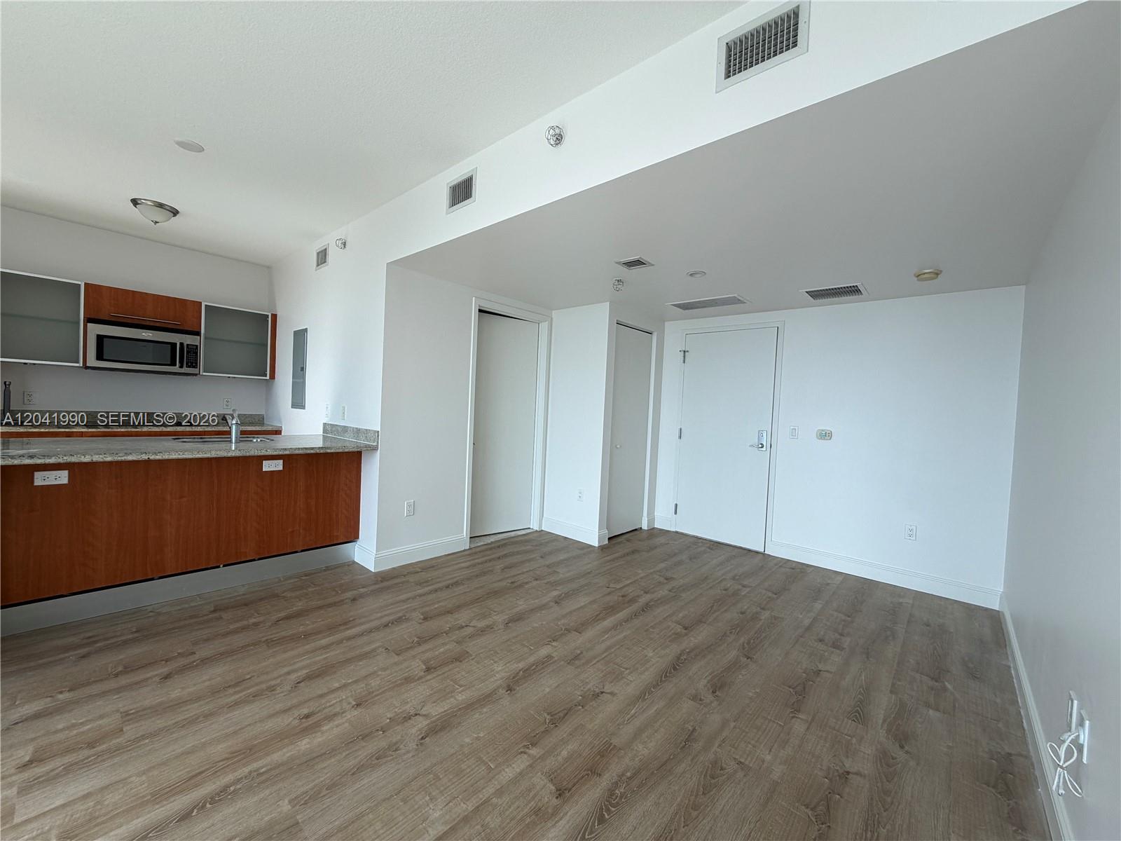 A kitchen with wood cabinets and a granite countertop opens into an empty living area — 185 SW 7th St # 3200, Miami FL 33130, MIAMI, FL