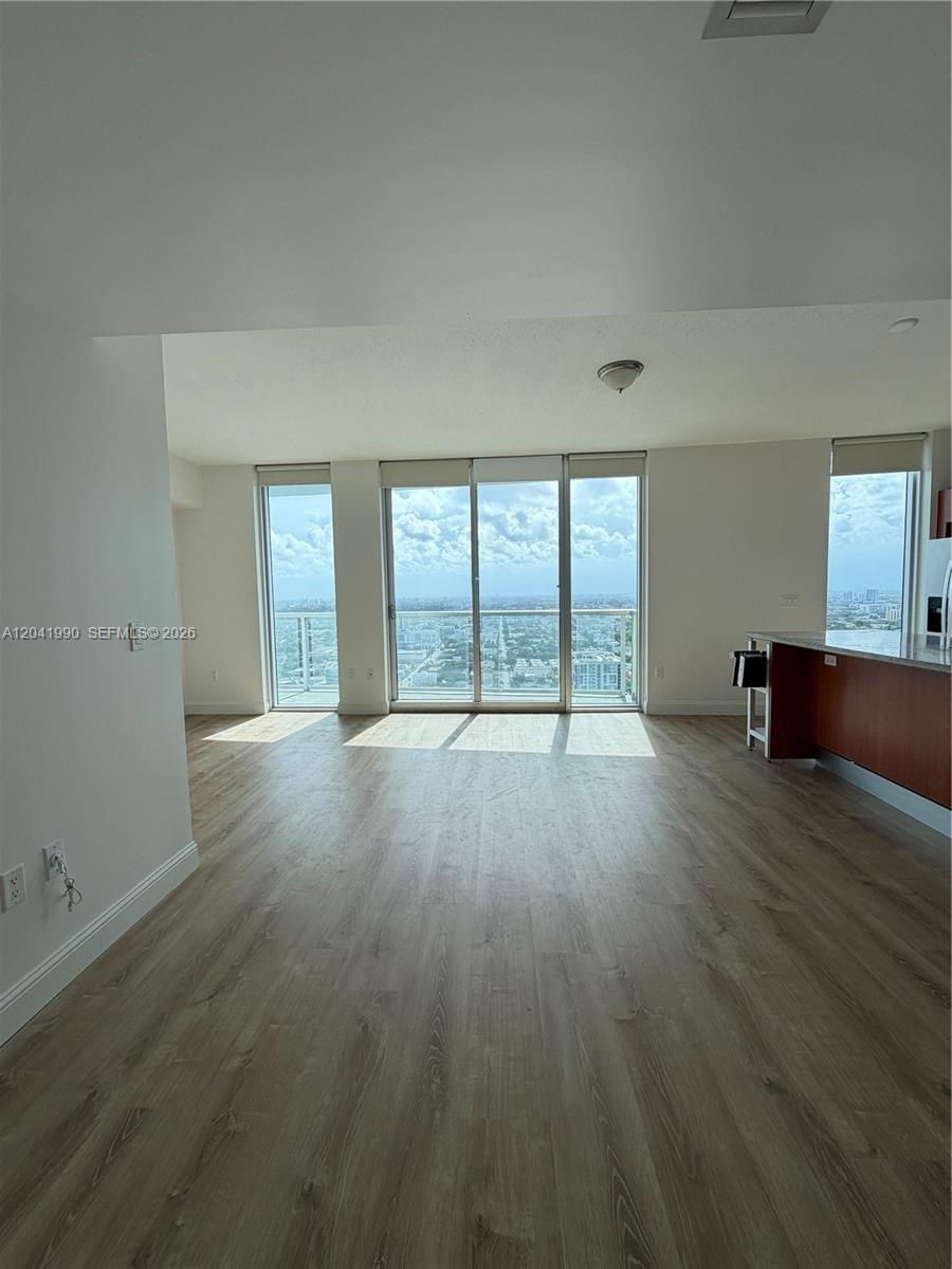 An empty living area features light wood-look flooring, floor-to-ceiling windows, and a kitchen island — 185 SW 7th St # 3200, Miami FL 33130, MIAMI, FL