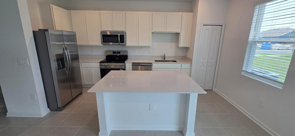 A kitchen features white cabinets, stainless steel appliances, a center island, and tile flooring — 6093 ZEN WAY, CLERMONT, FL