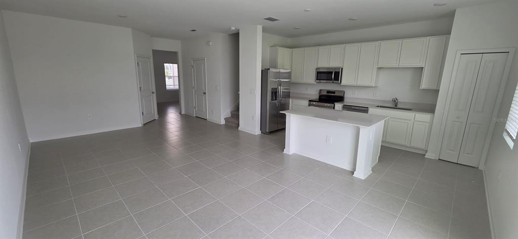 An open-concept kitchen and living area features white cabinets, stainless steel appliances, and tile flooring — 6093 ZEN WAY, CLERMONT, FL