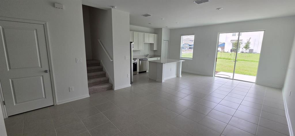 An open-concept kitchen and living area with tile floors, white cabinetry, and a sliding door — 6093 ZEN WAY, CLERMONT, FL