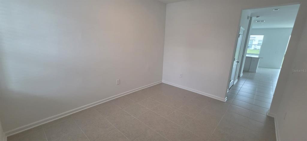 An empty room with light-colored walls and tile flooring leads to an adjacent living area — 6093 ZEN WAY, CLERMONT, FL