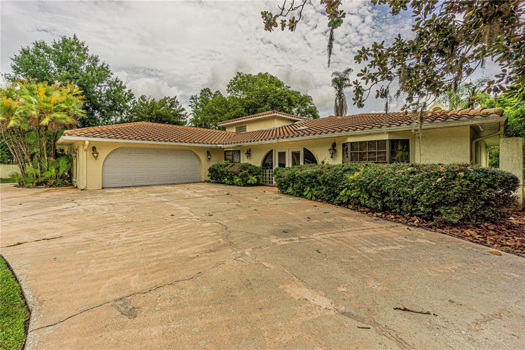 A single-story house with a tile roof, a large garage, and a cracked concrete driveway — 18129 CRAWLEY ROAD, ODESSA, FL