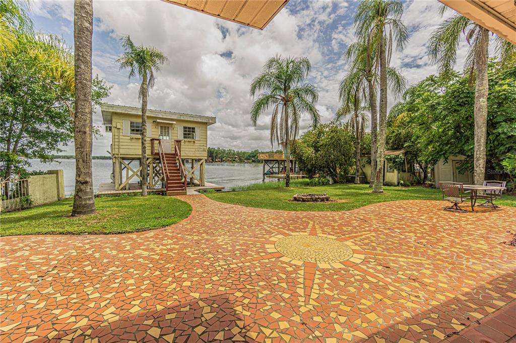 A patio with a mosaic sun design overlooks a lake, palm trees, and a stilt house — 18129 CRAWLEY ROAD, ODESSA, FL
