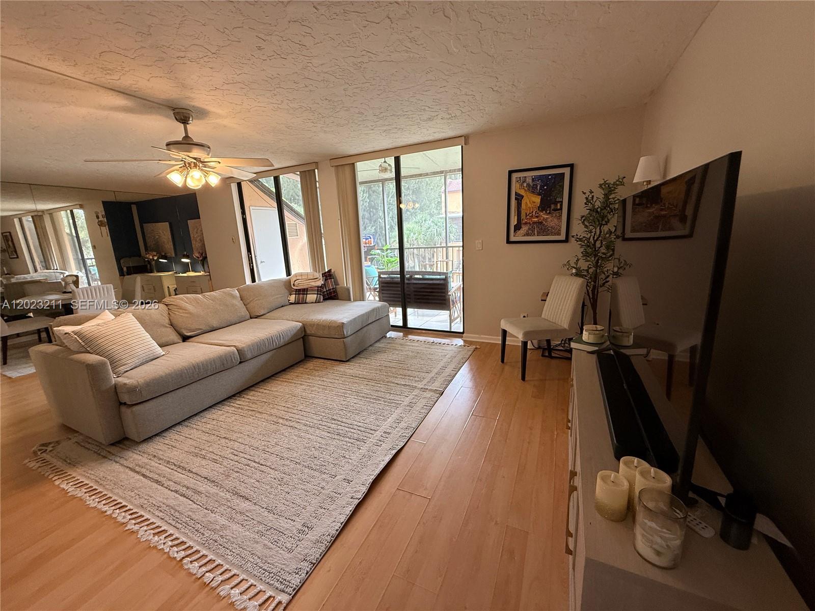 A living room features a sectional sofa, area rug, television, and sliding glass balcony doors — 450 Commodore Dr # 306, Plantation FL 33325, PLANTATION, FL