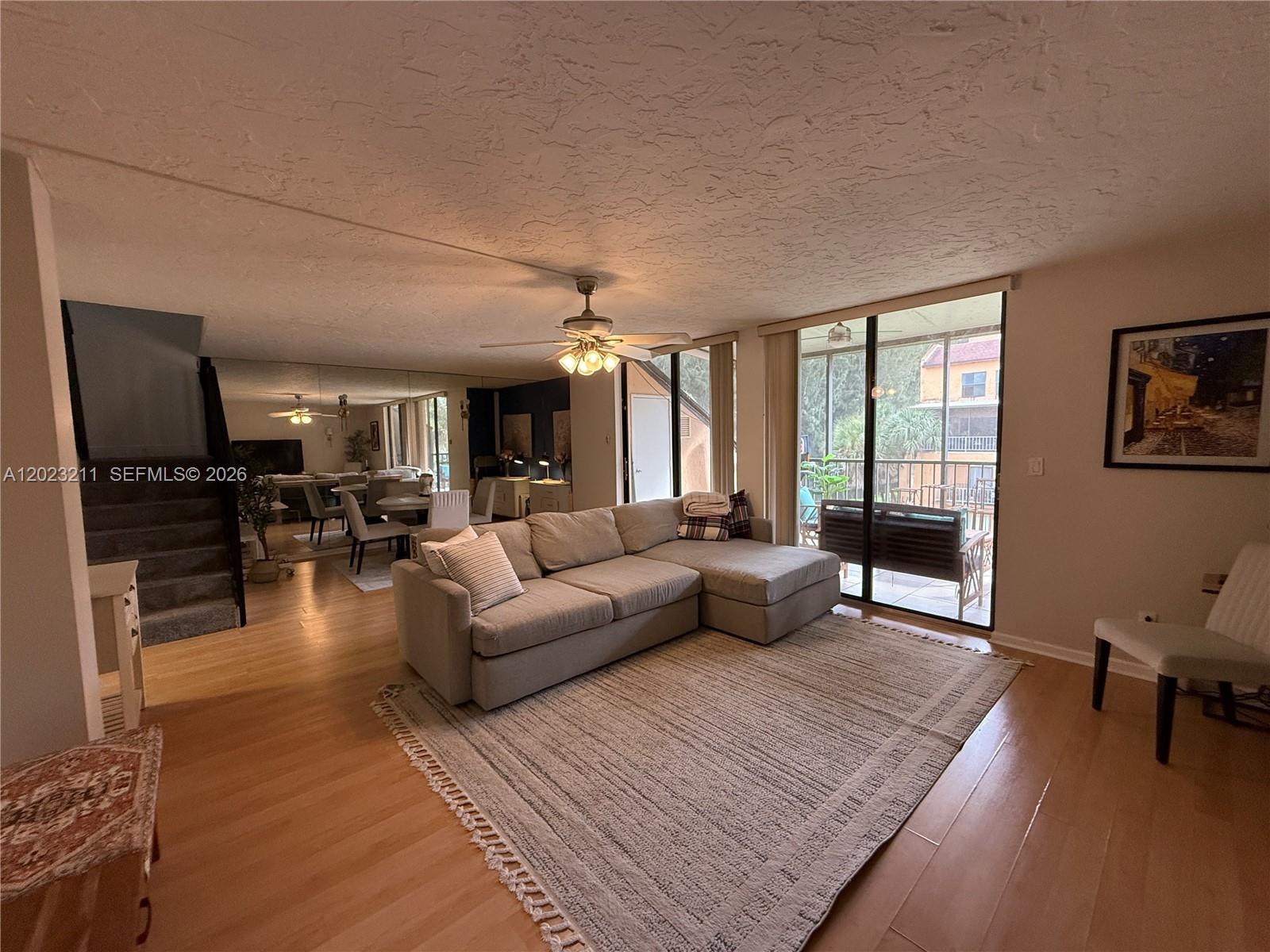 A living room features a sectional sofa, hardwood floors, a ceiling fan, and sliding doors — 450 Commodore Dr # 306, Plantation FL 33325, PLANTATION, FL