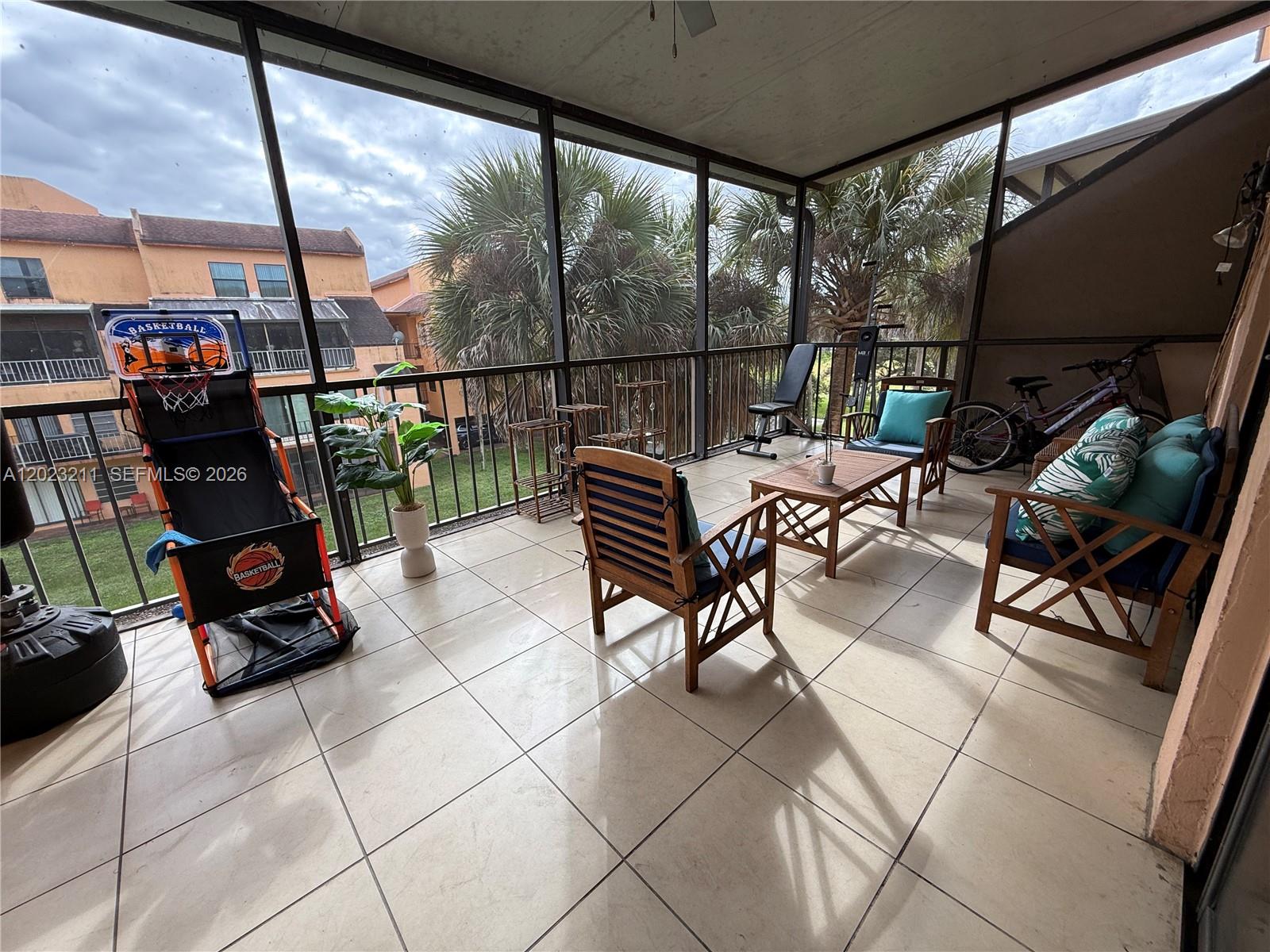 A screened-in balcony features tiled flooring, outdoor furniture, a basketball game, and palm trees outside — 450 Commodore Dr # 306, Plantation FL 33325, PLANTATION, FL