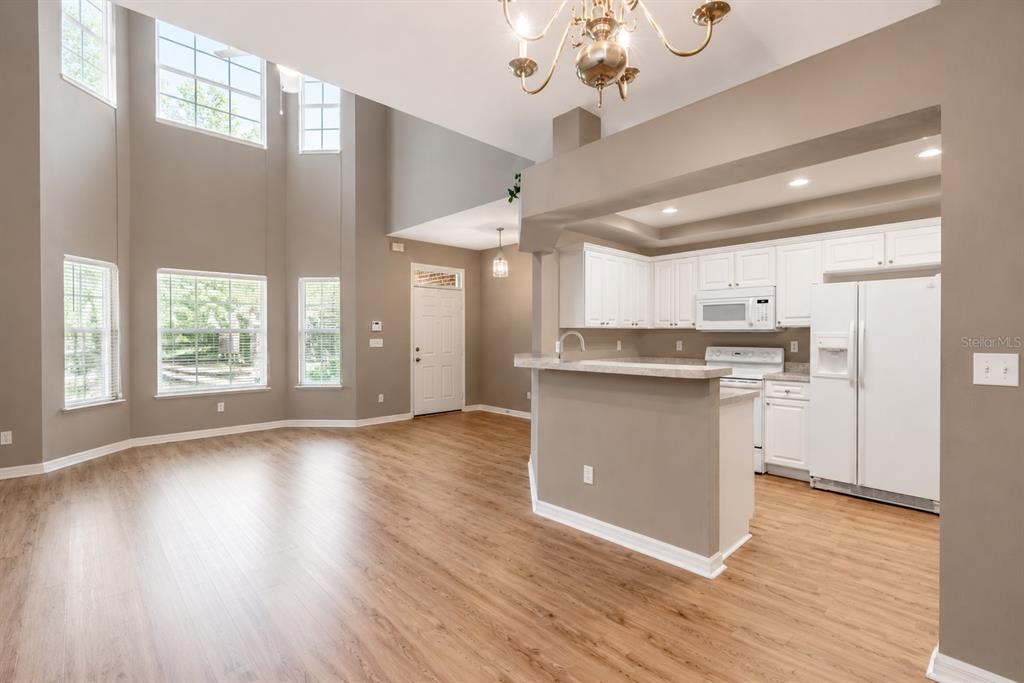 A bright living area with high ceilings and wood-look flooring opens to a white kitchen — 4946 NW 1ST PLACE, GAINESVILLE, FL