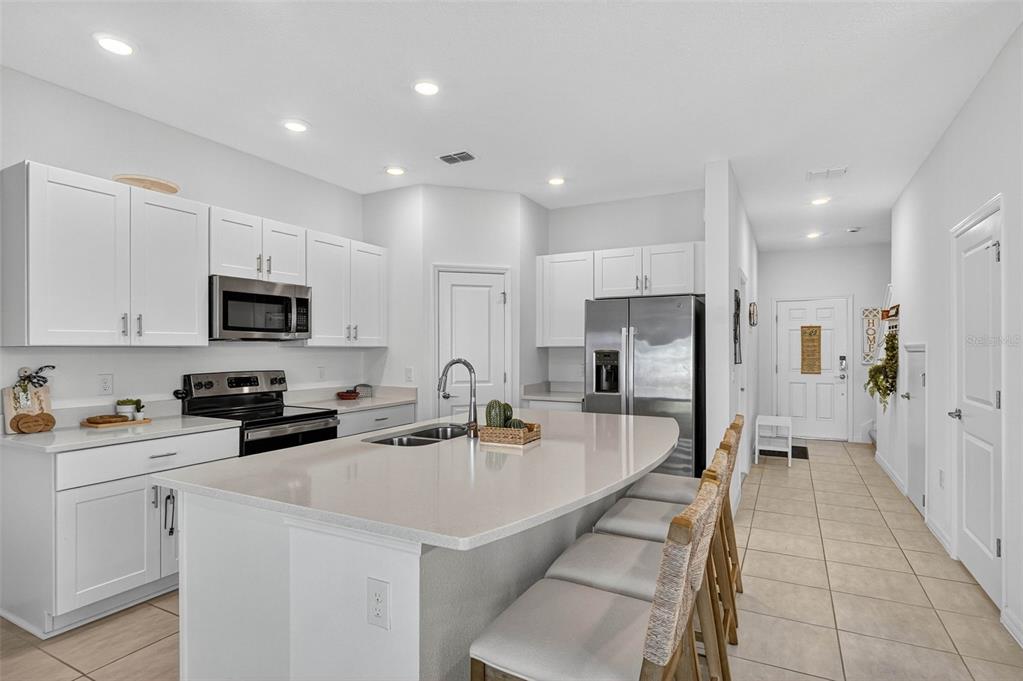 A modern kitchen features white cabinetry, quartz countertops, a central island, and stainless steel appliances — 3607 MAIN HARBOR DRIVE S, KISSIMMEE, FL