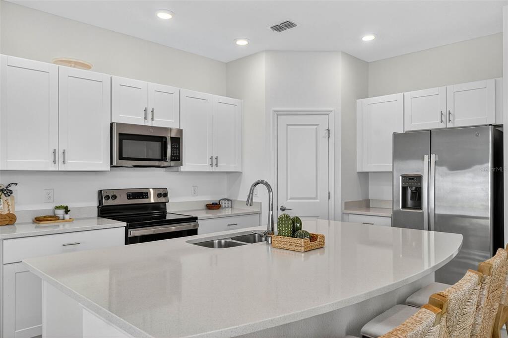 A modern kitchen features white cabinets, stainless steel appliances, and a large quartz-topped island — 3607 MAIN HARBOR DRIVE S, KISSIMMEE, FL