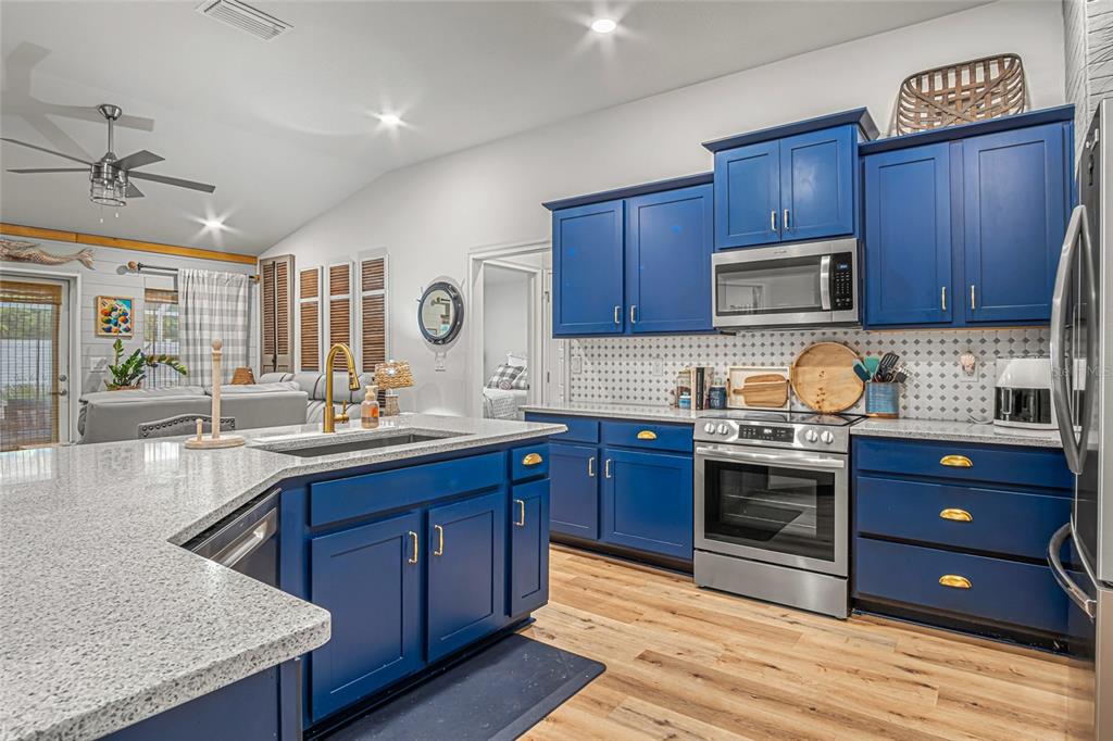A kitchen features blue cabinets, granite countertops, stainless steel appliances, and light wood flooring — 771 TUPELO CIRCLE, COCOA, FL