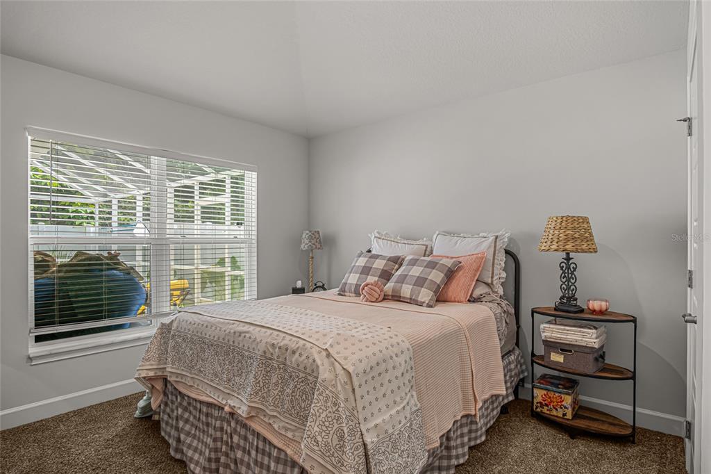 A bedroom features a bed with patterned bedding, a window with blinds, and a side table — 771 TUPELO CIRCLE, COCOA, FL