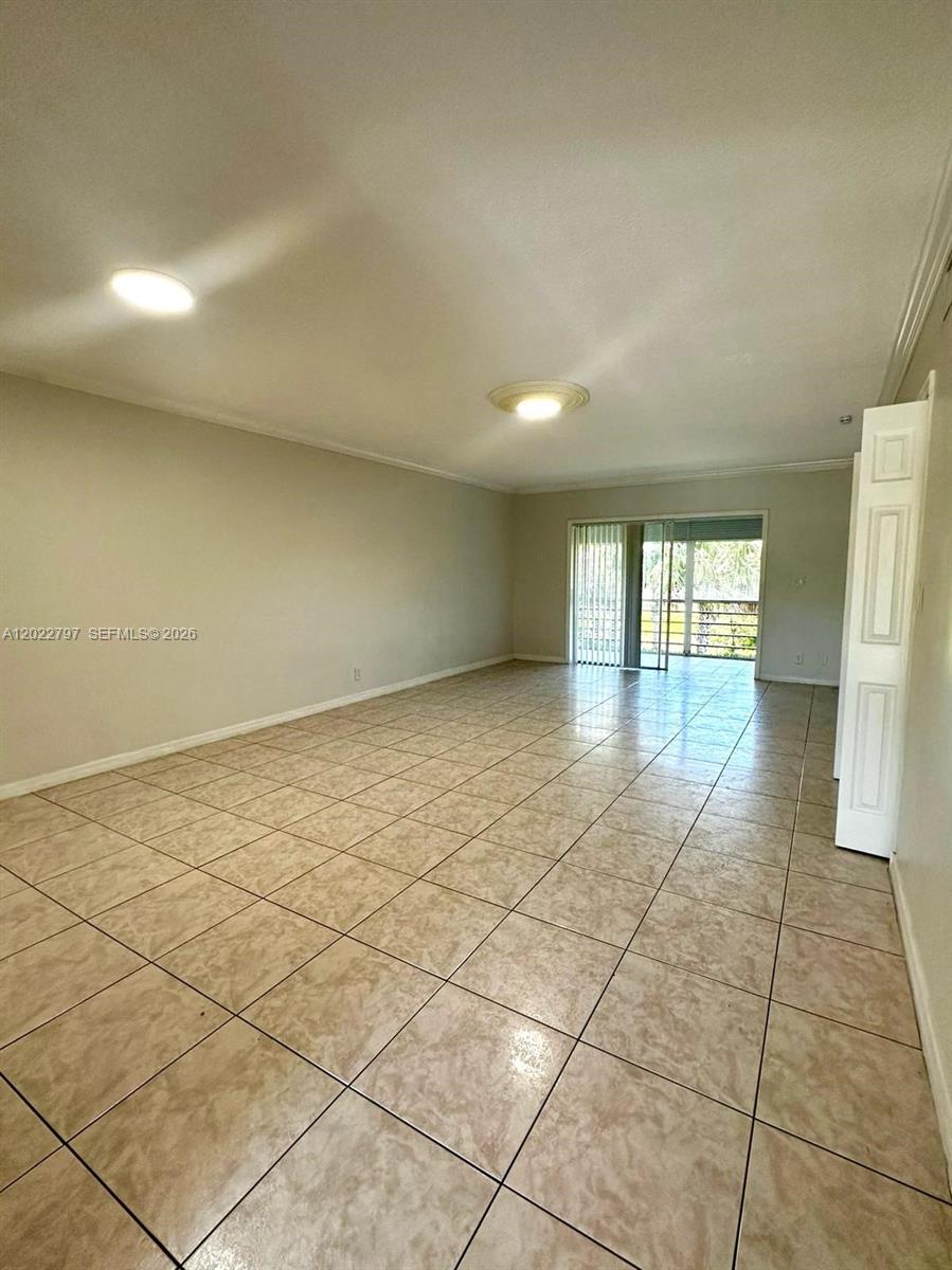An empty room features beige tile flooring, white walls, and a sliding glass door — 4291 NW 9th Ave # 202, Deerfield Beach FL 33064, DEERFIELD BEACH, FL
