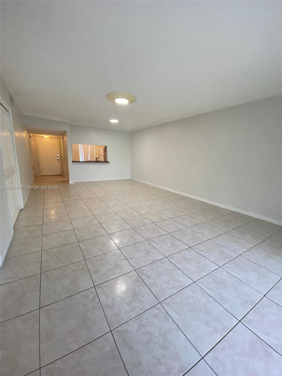 An empty living room features light-colored floor tiles, white walls, and a kitchen pass-through window — 4291 NW 9th Ave # 202, Deerfield Beach FL 33064, DEERFIELD BEACH, FL