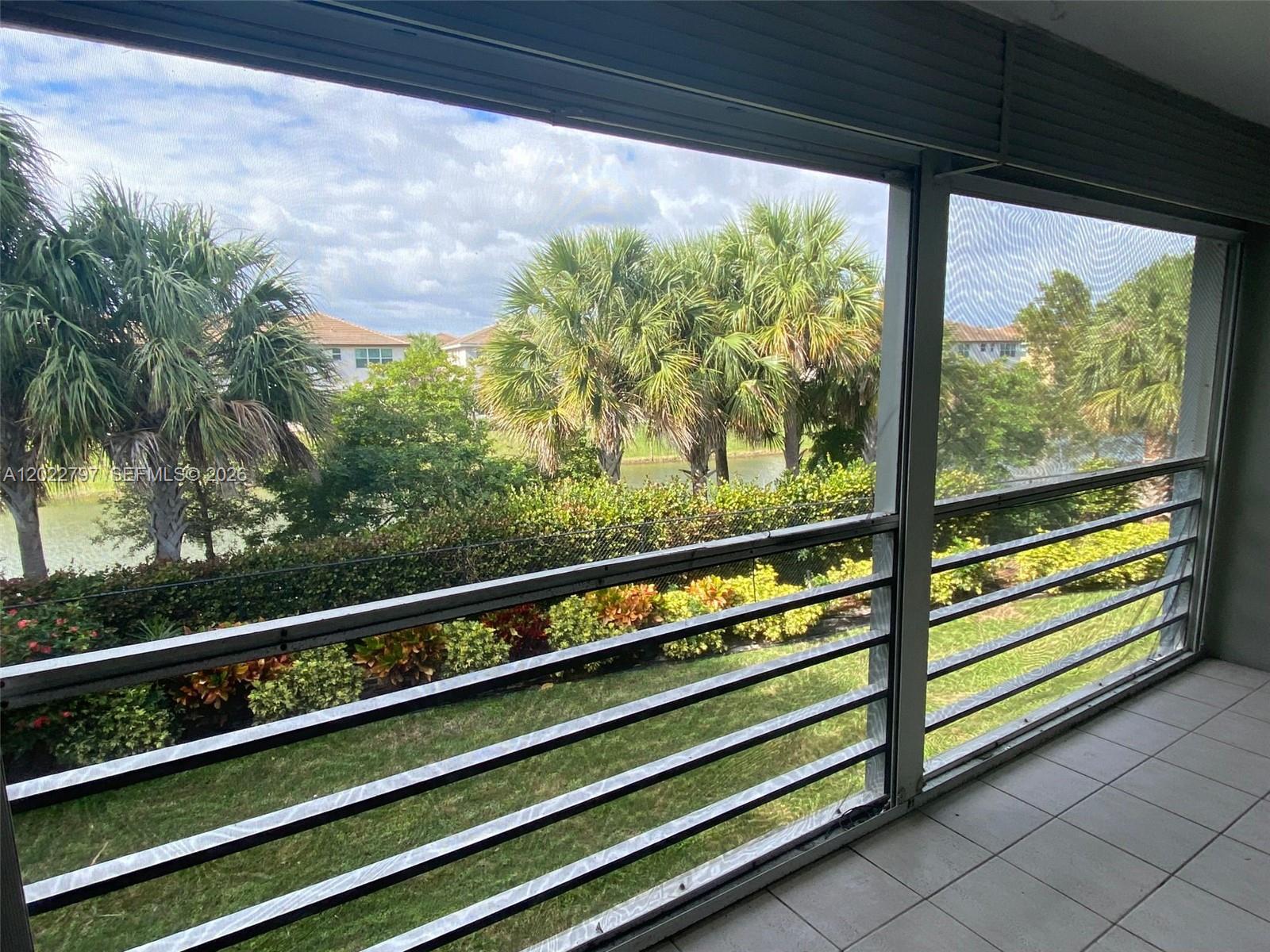 A screened-in balcony overlooks a grassy lawn, palm trees, and a small pond — 4291 NW 9th Ave # 202, Deerfield Beach FL 33064, DEERFIELD BEACH, FL