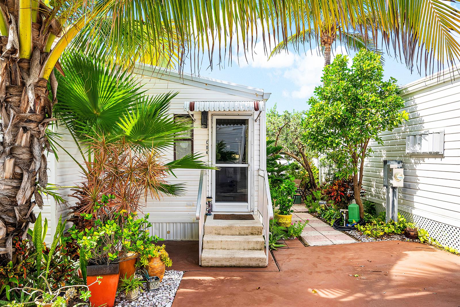 A white mobile home with a front porch, stairs, and lush tropical landscaping — 4 East Cedar Drive, Briny Breezes FL 33435, BRINY BREEZES, FL
