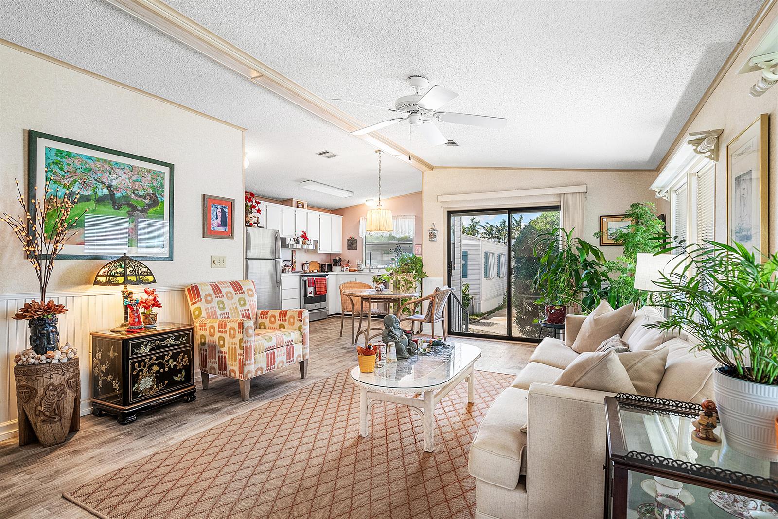 A living room with a beige sofa, patterned armchair, glass coffee table, and open kitchen — 4 East Cedar Drive, Briny Breezes FL 33435, BRINY BREEZES, FL